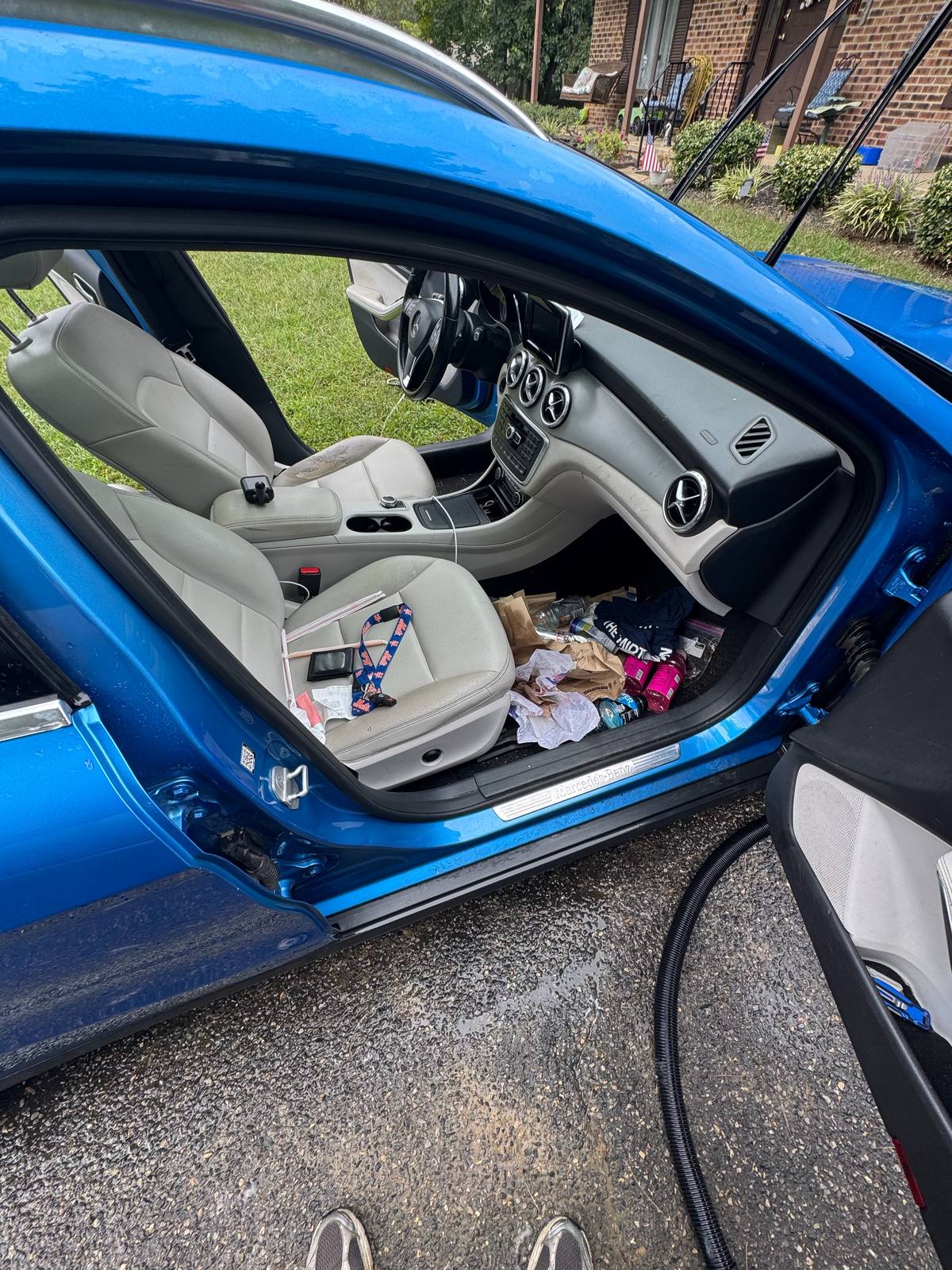 Mercedes-Benz passenger footwell before detailing, with trash, bottles, and clutter on the floor and seat.